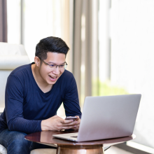 PCで試合観戦をしながらスマートフォンを操作している笑顔の男性